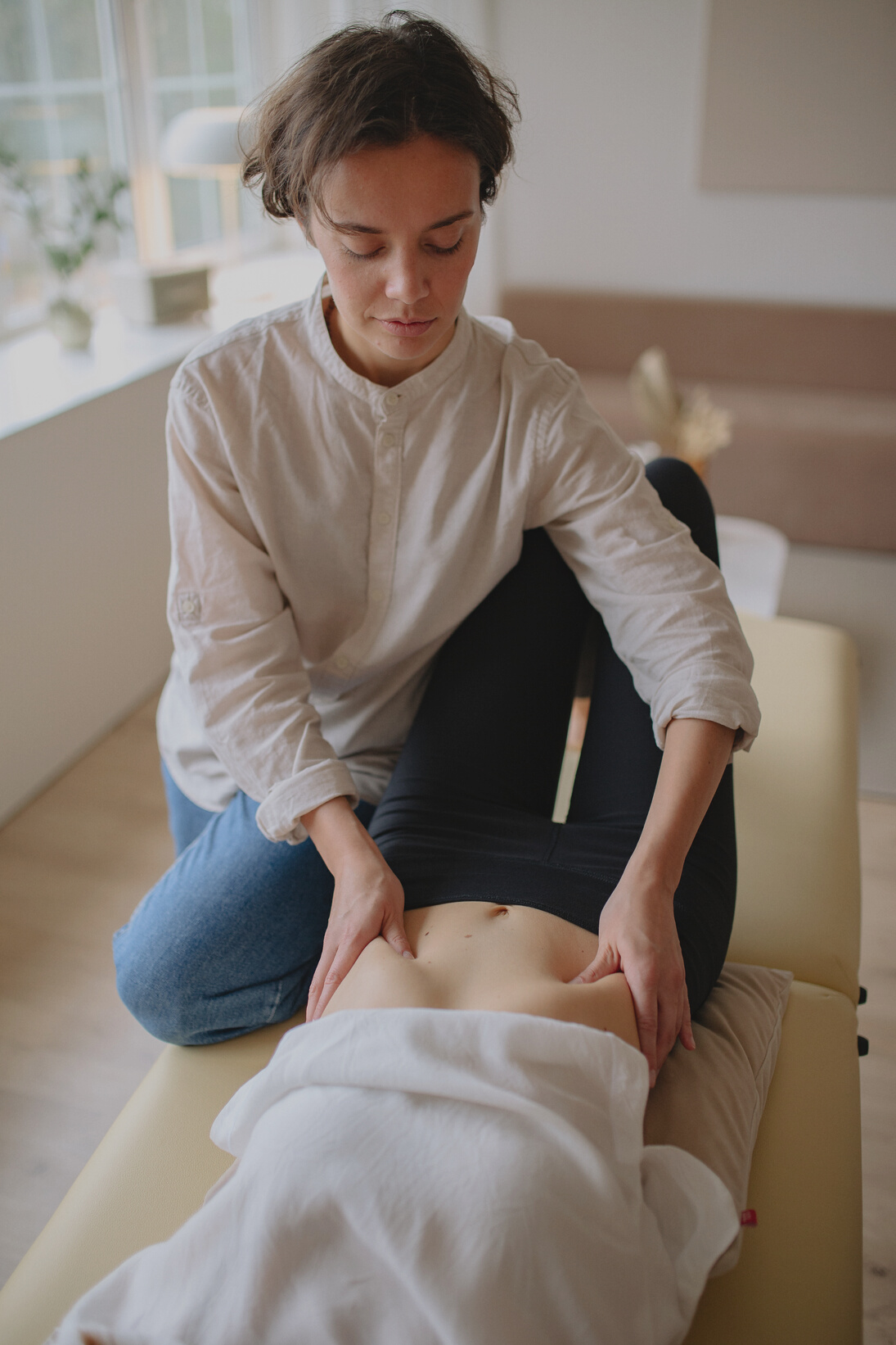 A Woman in White Top Massaging a Person's Belly